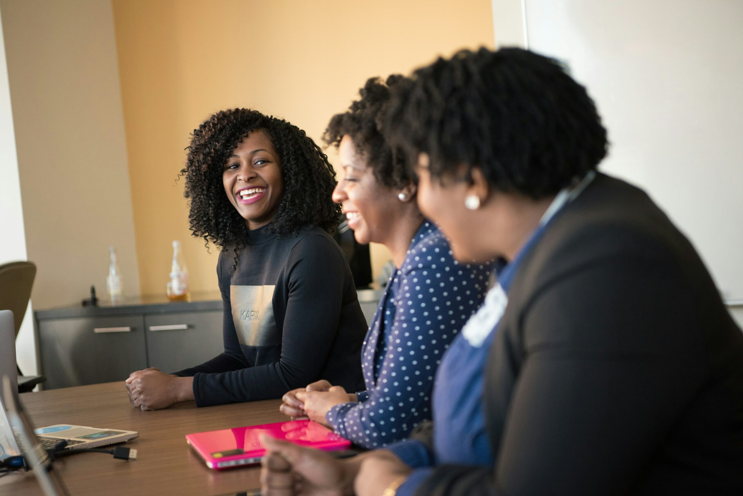 Trois femmes professionnelles échangent en confiance, représentant un annuaire humain dédié à l’accompagnement du burn-out. Trois femmes souriantes en pleine discussion, illustrant l’échange et le soutien entre professionnels